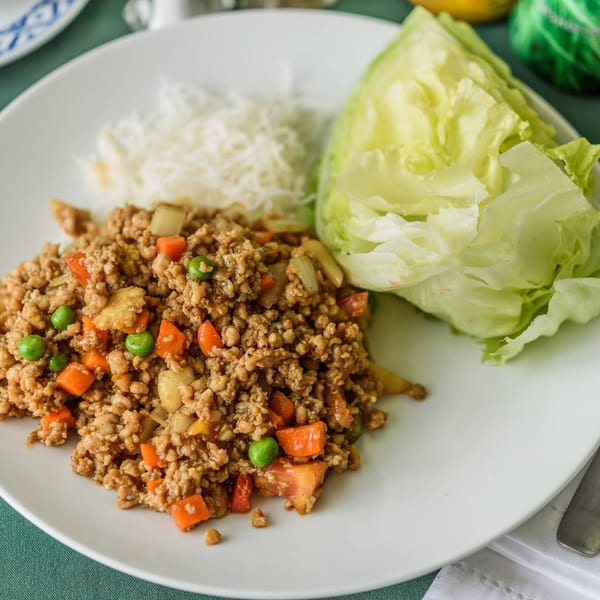 Thai Larb Gai with minced chicken, carrots, peas, and lettuce wraps on a white plate.