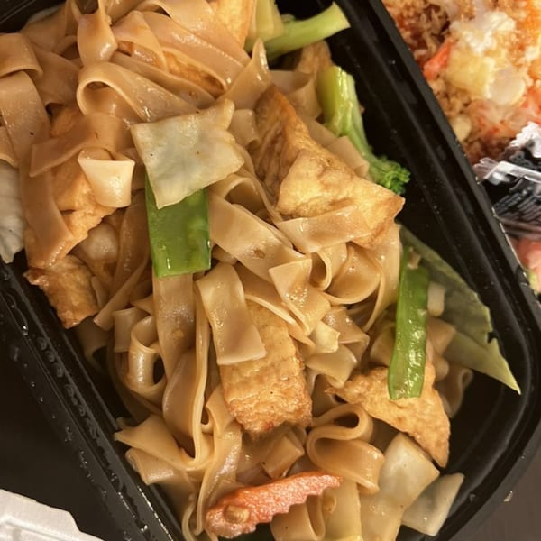 Close-up of Thai drunken noodles with tofu, broccoli, and green beans in a black container.