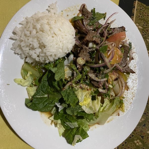 Thai beef salad with onions, tomatoes, and herbs, served with a side of white rice.
