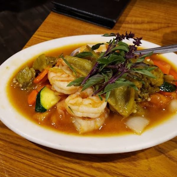 Shrimp and vegetables in a rich orange sauce, garnished with fresh basil, on a white plate.