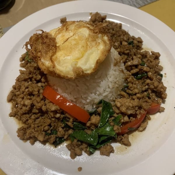 Thai basil chicken with rice, a fried egg, and red peppers on a white plate.