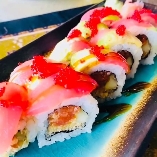 Colorful sushi rolls with pink fish, red roe, and yellow sauce on a blue and gold plate.