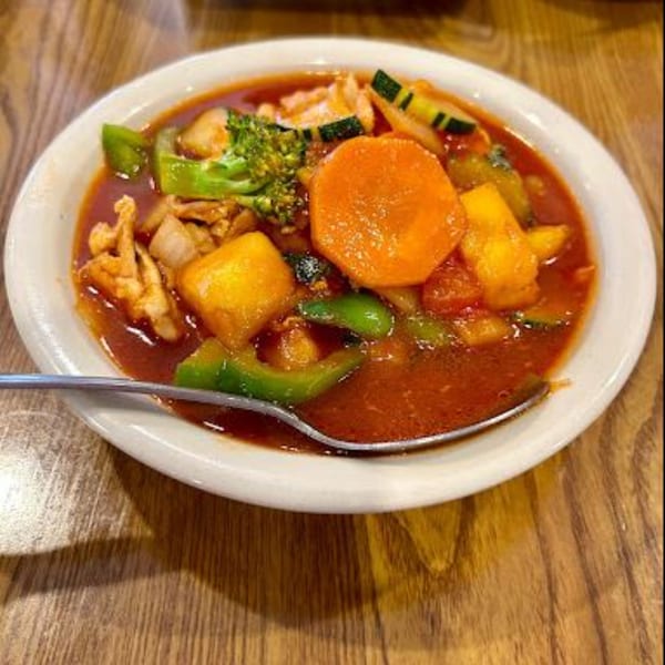 A bowl of Thai sweet and sour chicken with vegetables and a spoon on a wooden table.