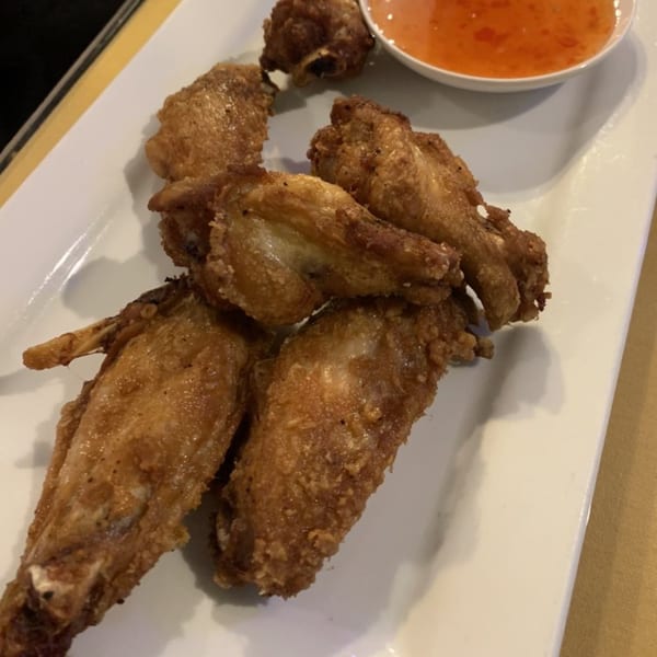 Crispy fried chicken wings with a side of sweet chili dipping sauce on a white rectangular plate.