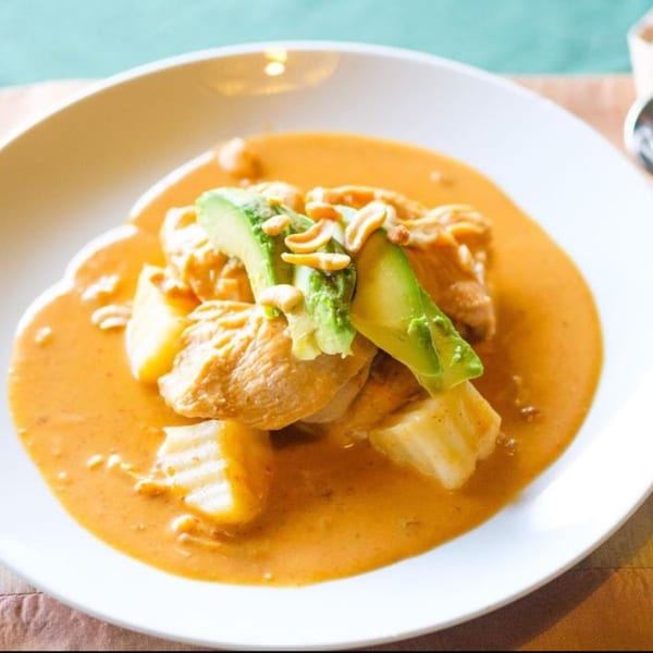 Thai Massaman curry with chicken, potatoes, avocado, and peanuts in a white bowl.